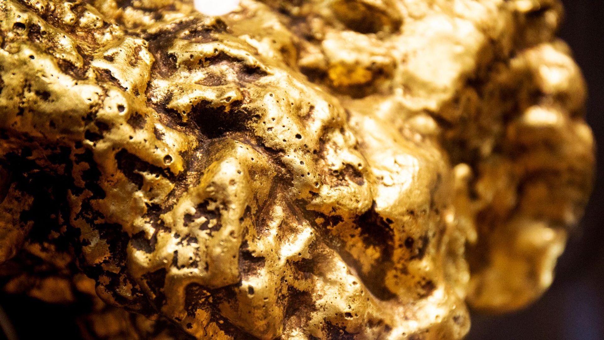 Close-up of a textured gold nugget with natural surface irregularities and shiny reflections.